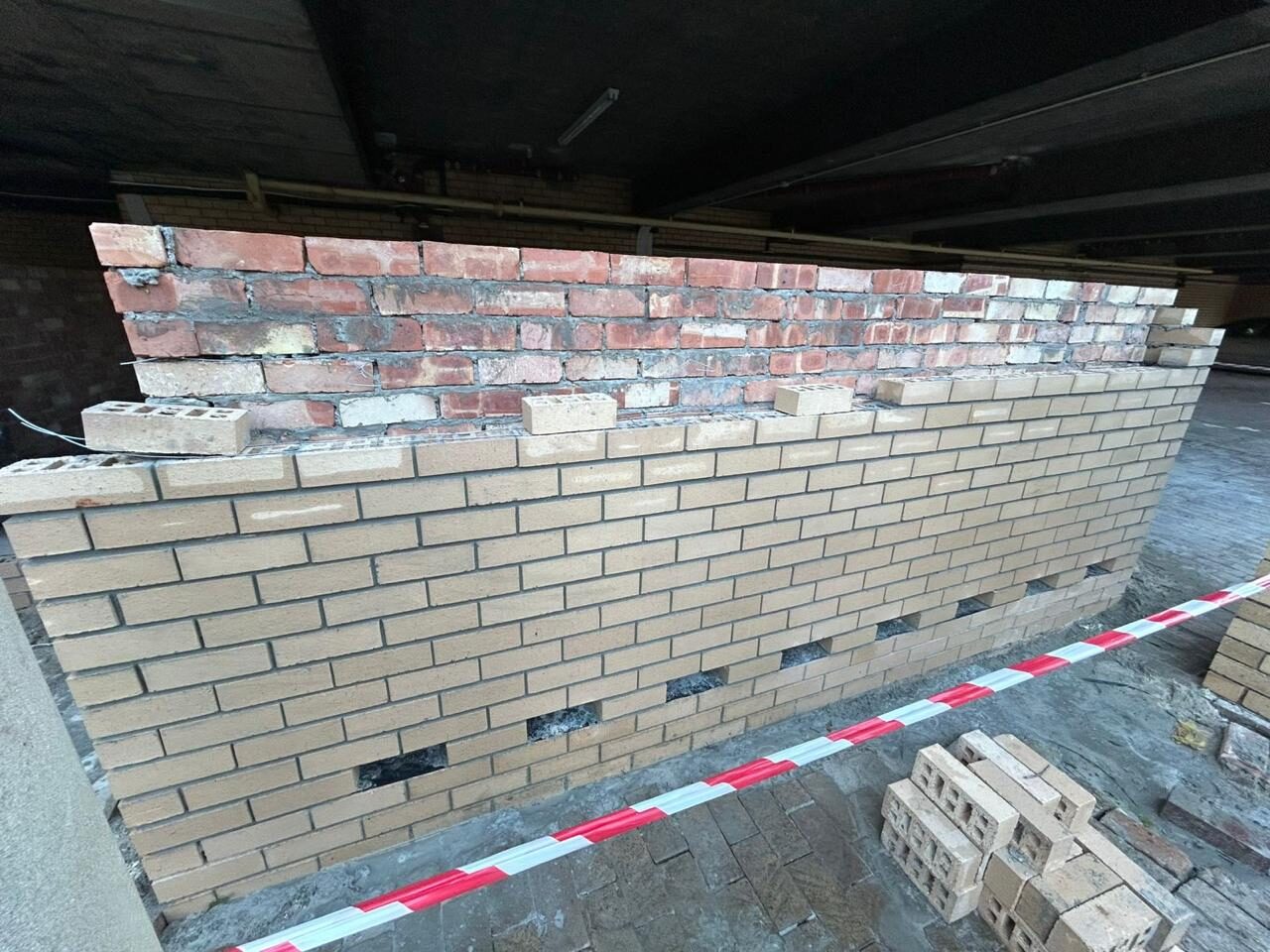 Face brickwork rising under the parking structure, toothed ends left for the next bay and weep holes set into the course