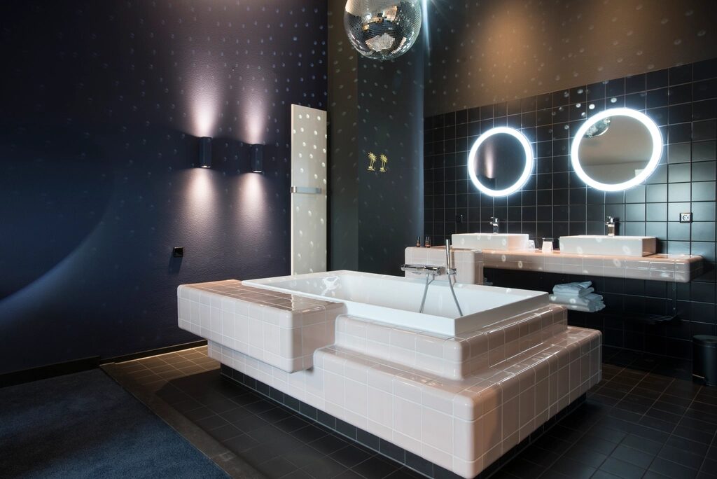 Indicative reference: a dark-tiled bathroom with twin wall-hung basins and backlit round mirrors