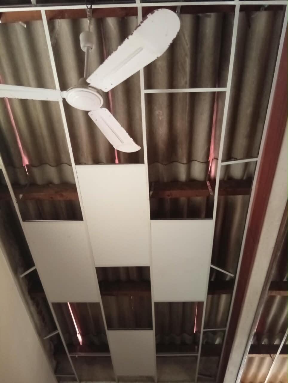 New ceiling boards being fixed into the suspended grid around an existing ceiling fan